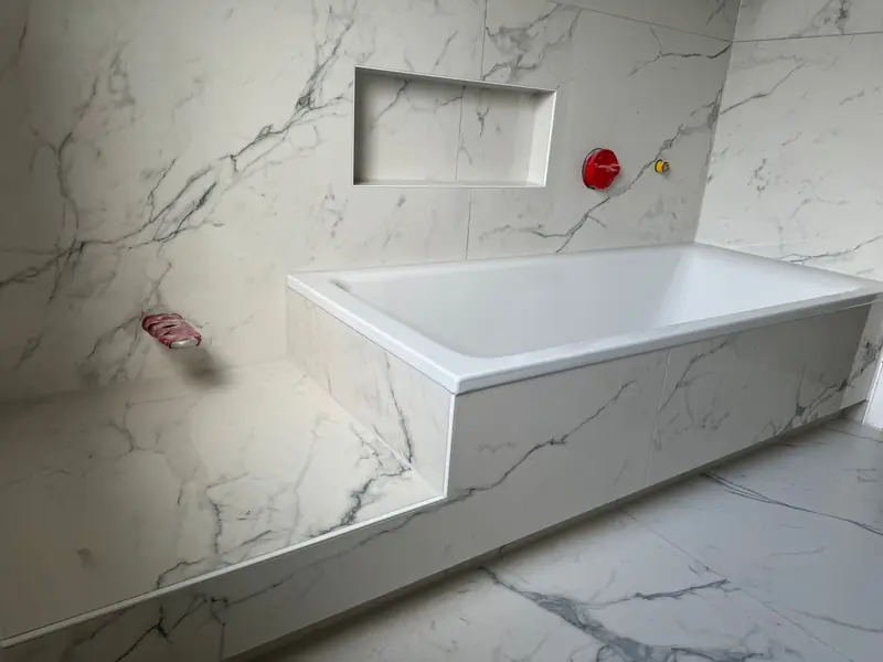 Badewanne mit Wannenverkleidung und Wandfliesen in Marmoroptik