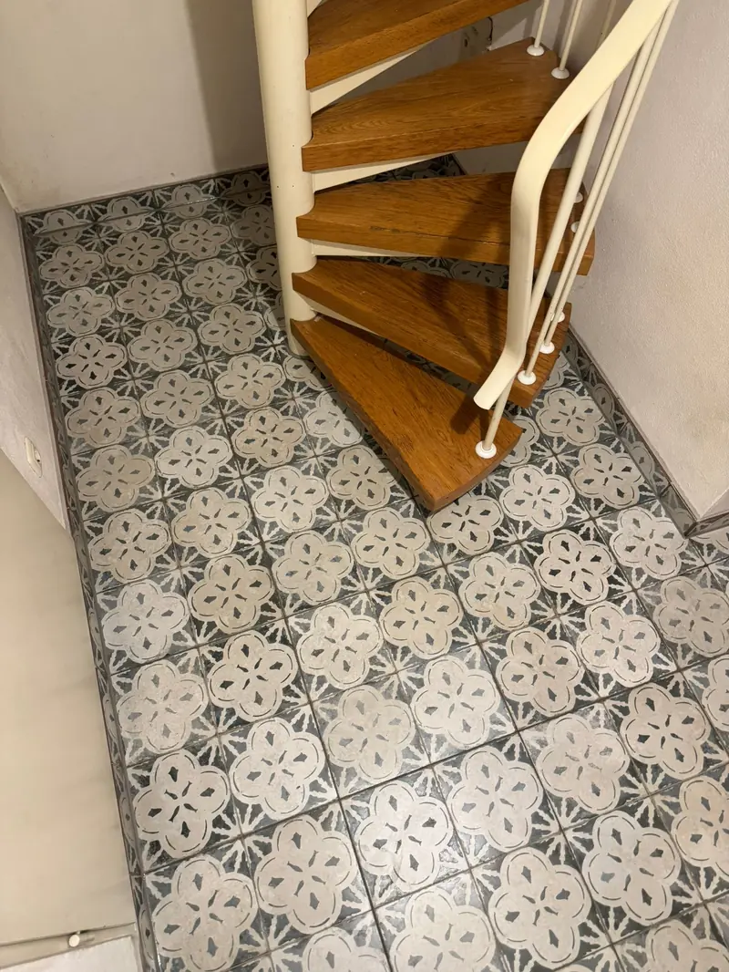 Fliesenboden mit Muster unter einer Wendeltreppe mit Holzstufen
