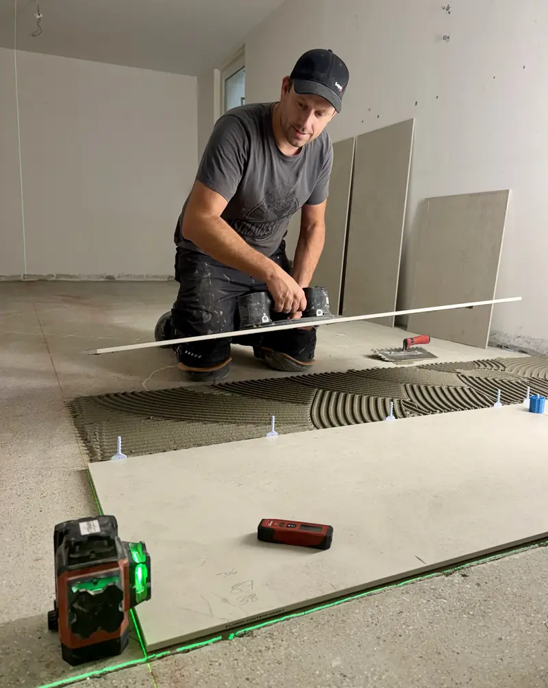 Fliesenleger prüft die Verlegefläche mit Richtlatte und Laser