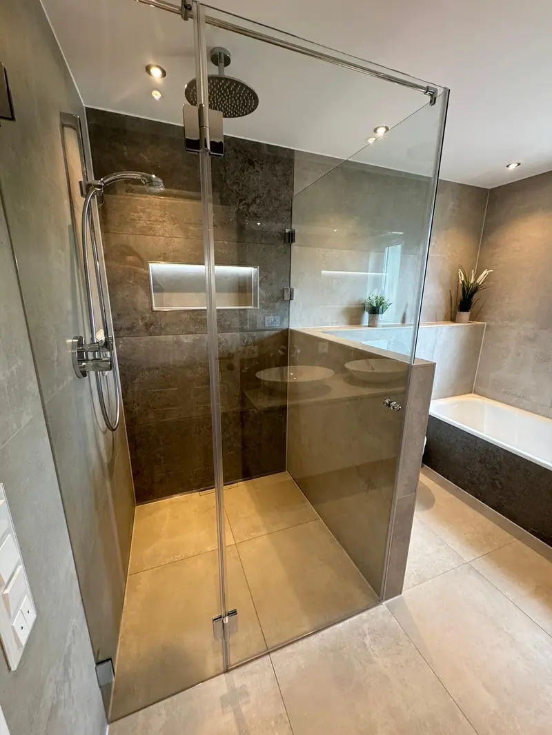 Glasdusche mit dunklen Wandfliesen, daneben eine Badewanne