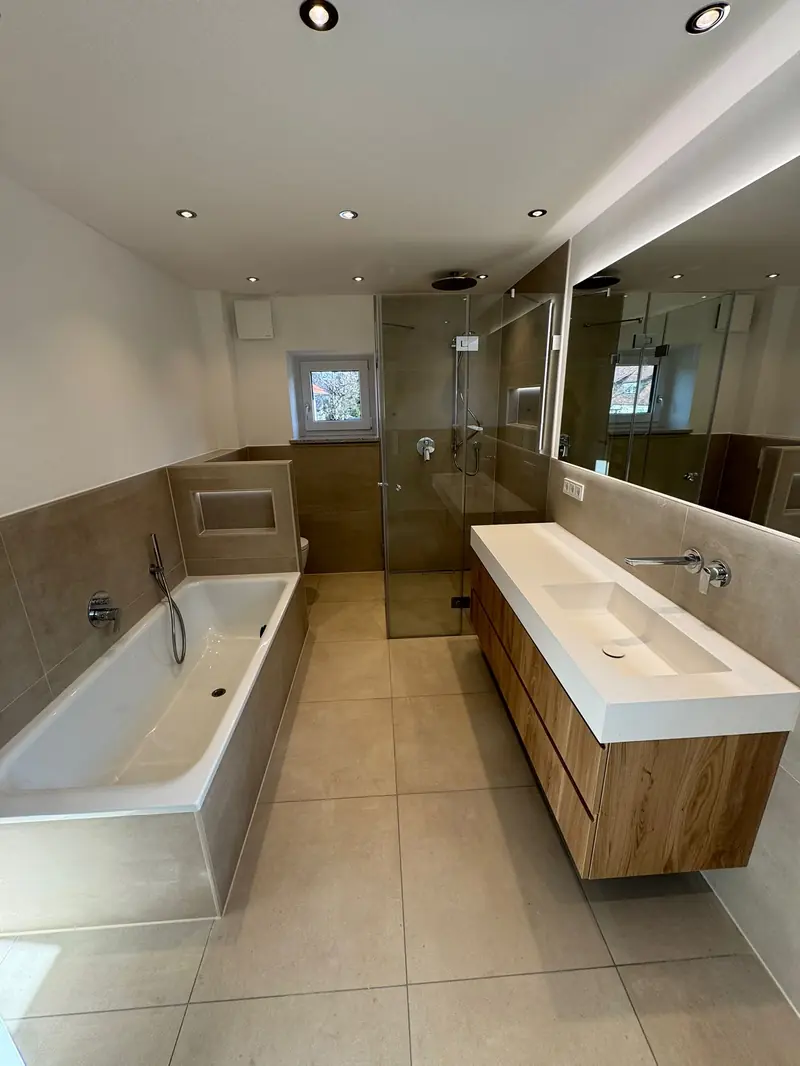 Helles Badezimmer mit Badewanne, Glasdusche und Waschtisch mit Holzfront